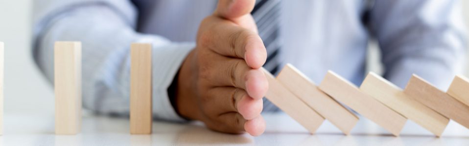 Hands of the young man prevent Dominoes from falling to reduce business risks ,Concepts and strategic plans to protect businesses for success.